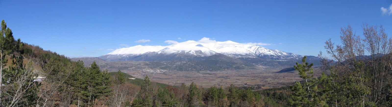 The southern peaks of Mount Olympus under snow, above wooded foothills and a wide valley